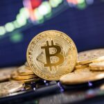 Moneta Bitcoin na monitorze z wykresem giełdowym